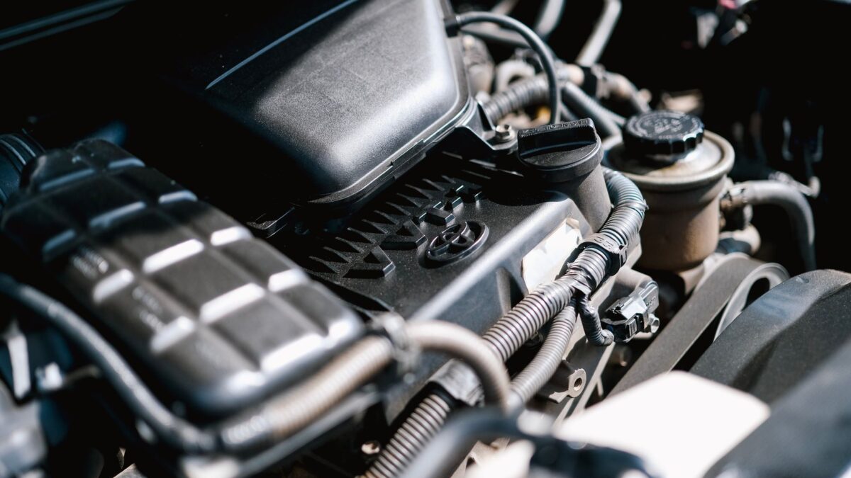 Plan rapproché du compartiment moteur d'une voiture, montrant des composants mécaniques comme des tuyaux, un réservoir de liquide et une couverture de moteur noire.