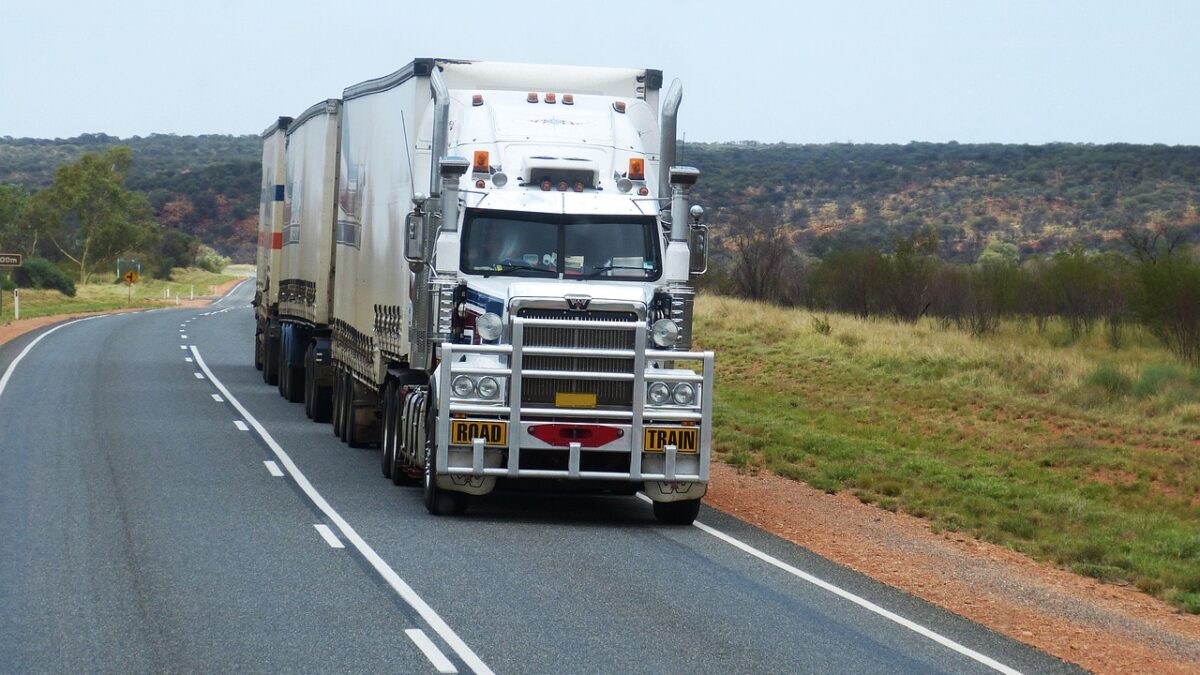 Un camion blanc de type road train roule sur une route australienne, entouré de savane et de végétation sèche.