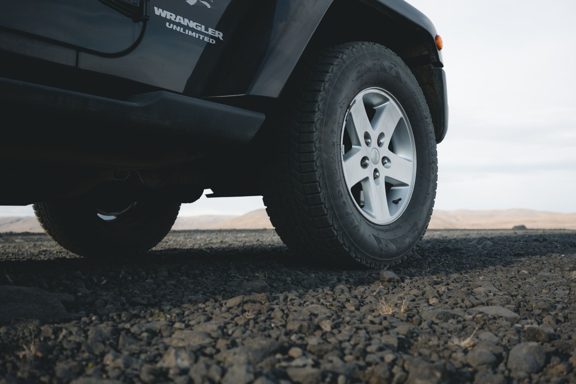 Close-up of an all-terrain tire and silver wheel on an off-road vehicle over rocky ground.