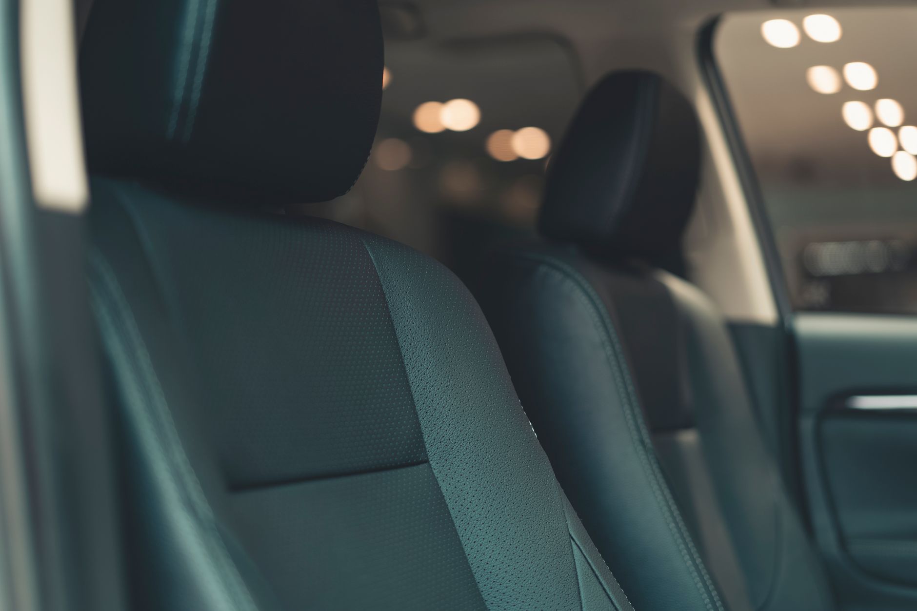Close-up view of dark perforated leather vehicle seats inside a modern automobile cabin.
