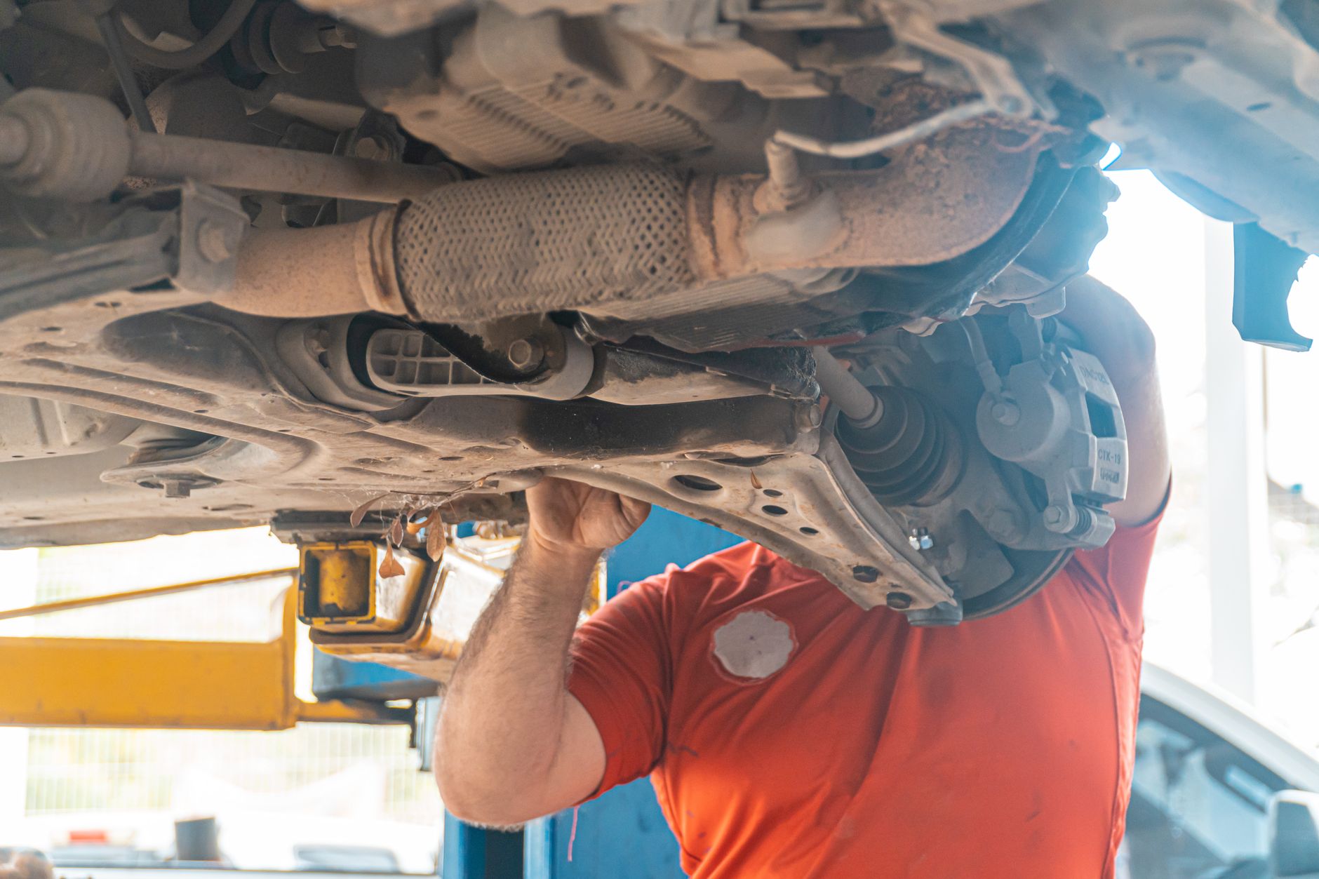Mechanic working on the undercarriage and suspension of an elevated vehicle.