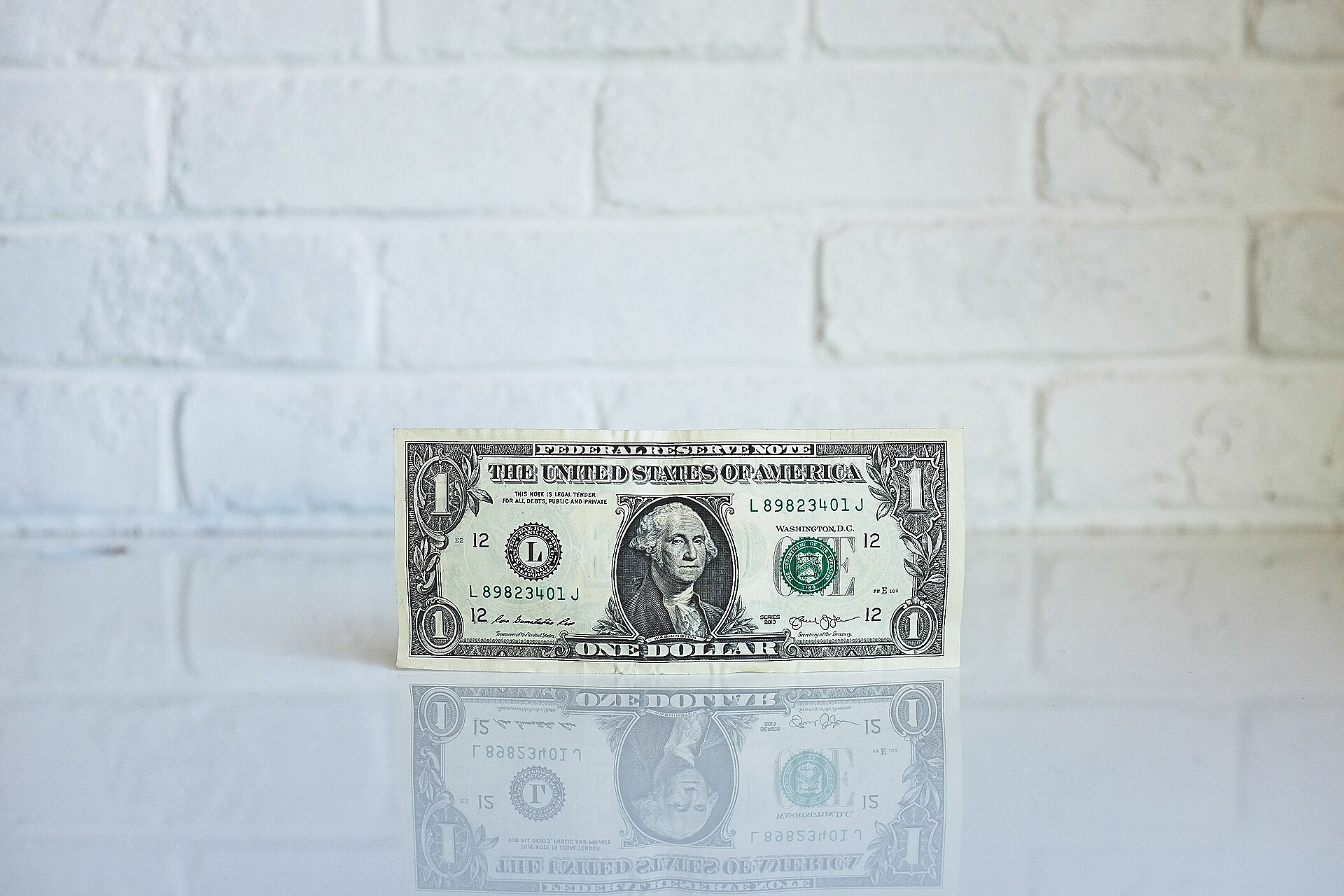 A single one dollar bill standing against a white brick wall