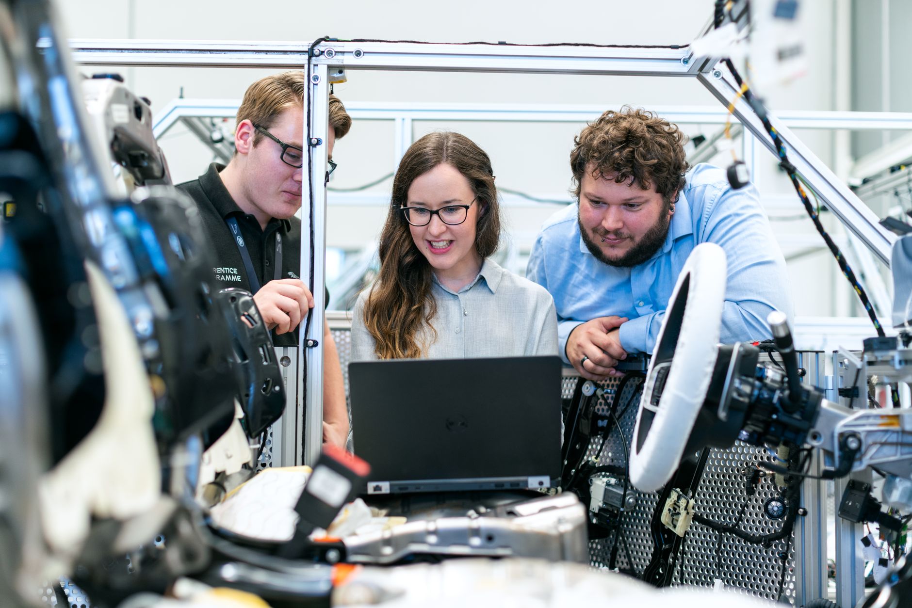 Three engineers look at a laptop beside a steering wheel test rig.