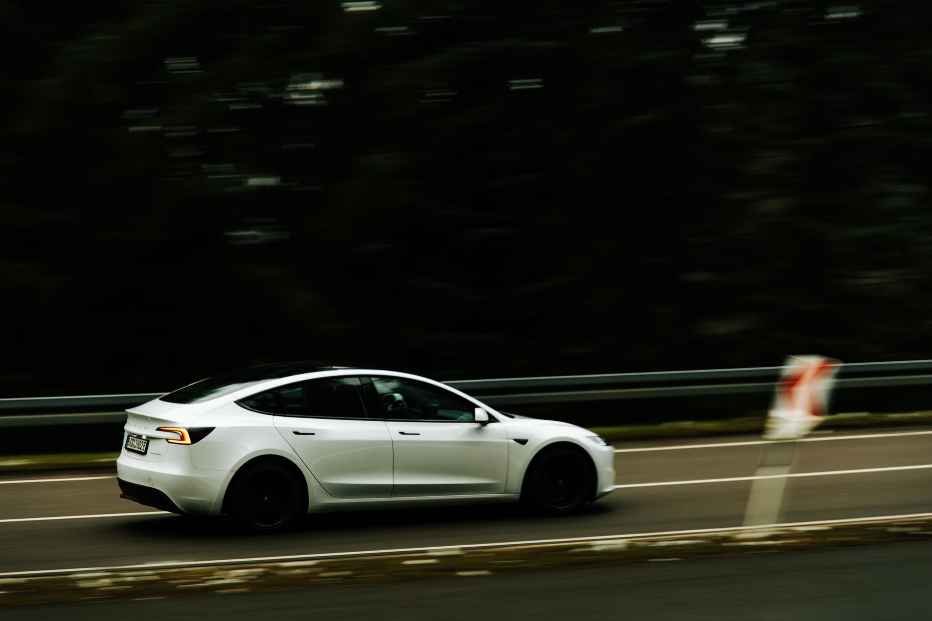 A white electric car drives at speed along a paved highway.